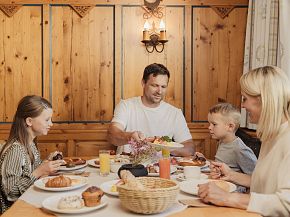 A family of four enjoying a meal together at a wooden table in a cozy dining room, surrounded by wooden panels and warm lighting.