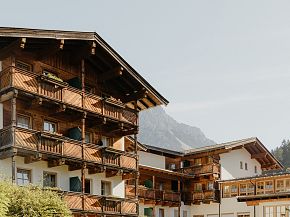 Traditional alpine hotel with wooden balconies set against a clear sky and mountain backdrop, reflecting a cozy and picturesque atmosphere.
