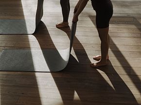 Zwei Personen rollen Yogamatten in einem lichtdurchfluteten Raum aus.